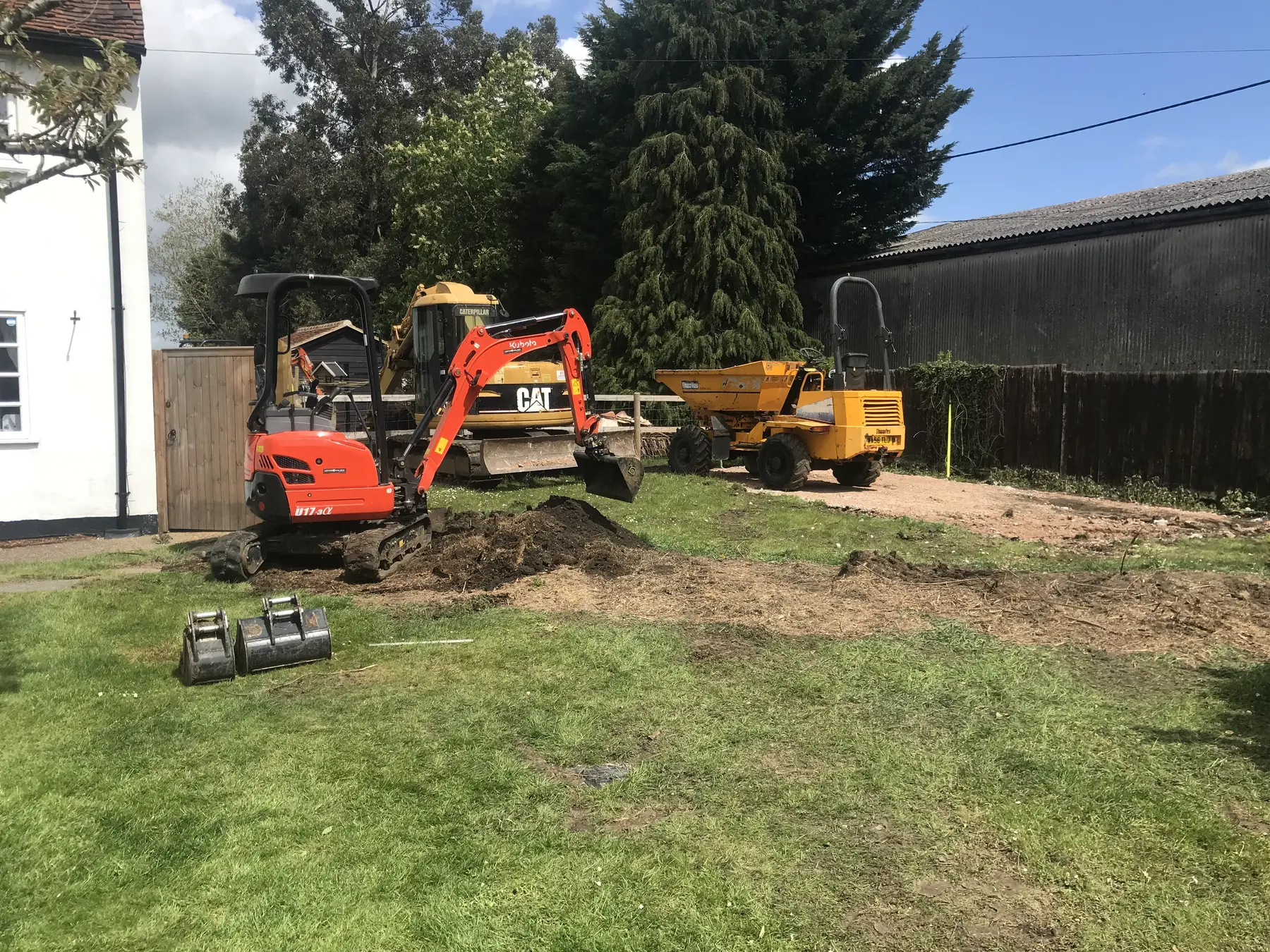 An orange micro excavator, a yellow excavator and a dumper at work on a cottage lawn.