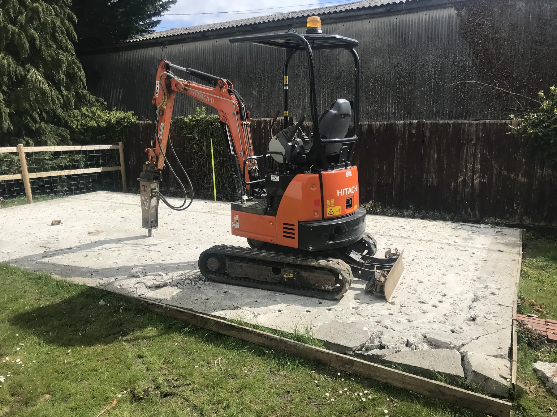 An orange micro excavator with a breaker on a concrete slab in a garden.