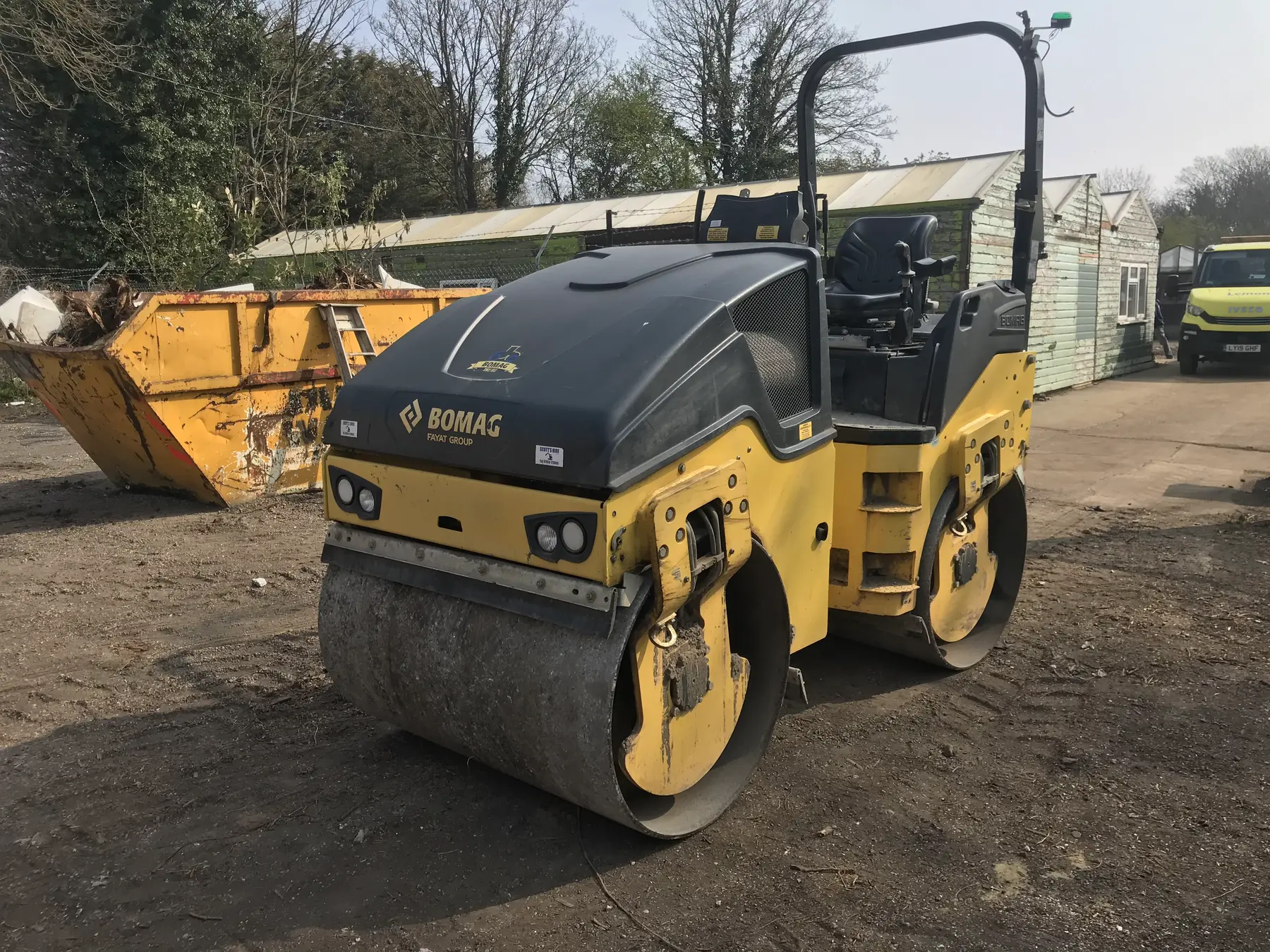 A yellow and black ride-on twin-drum roller on a gravel yard.